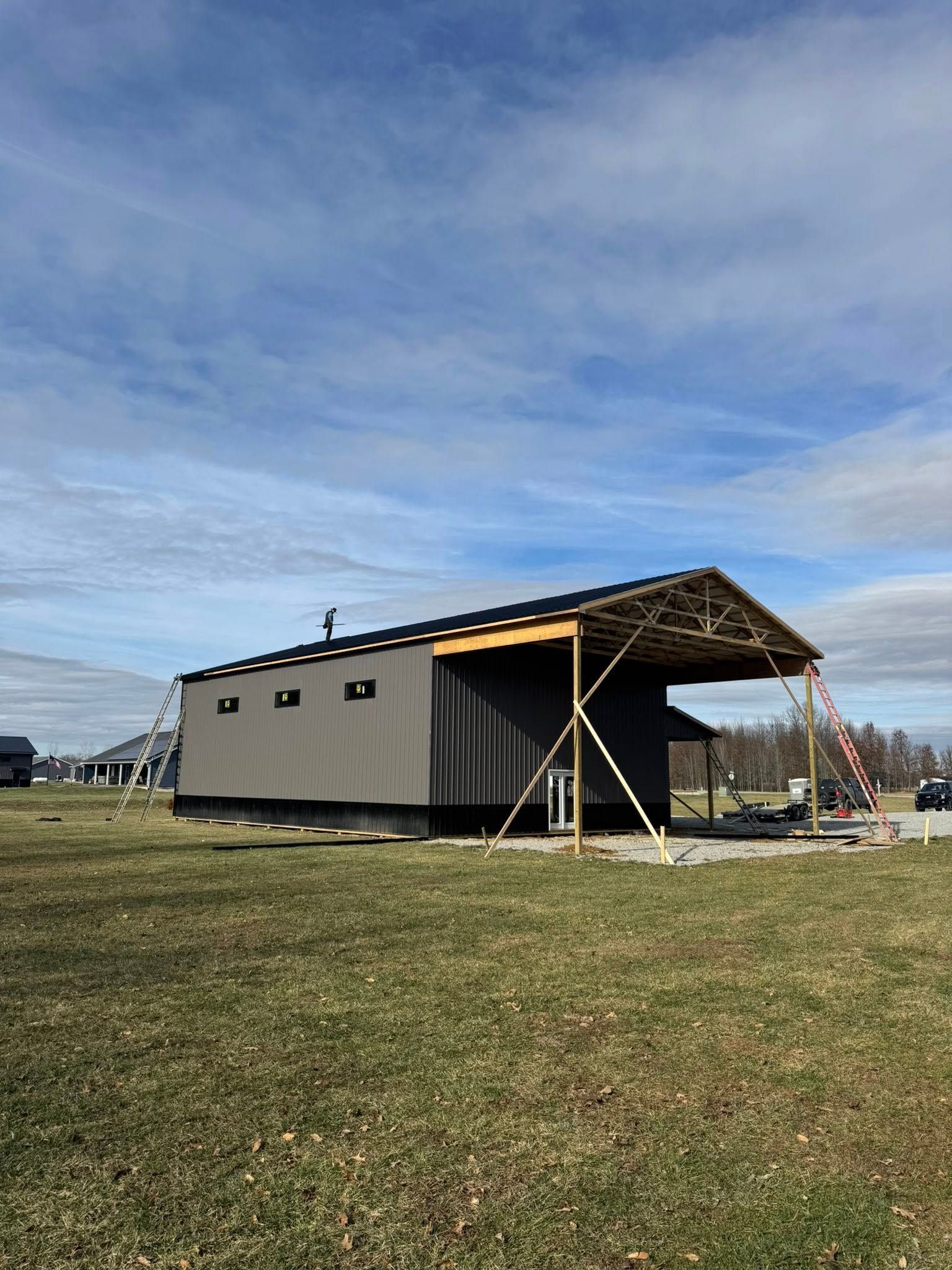 Portable tan shelter with black roof and support poles on a grassy field under a cloudy sky
