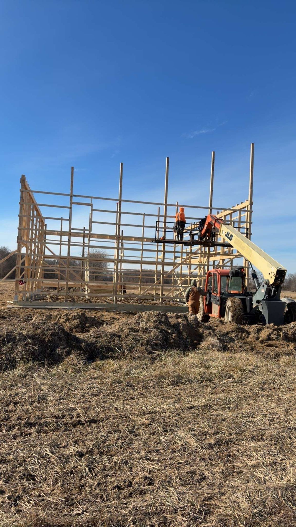 Construction workers on a wooden framework with a yellow lift under a clear blue sky