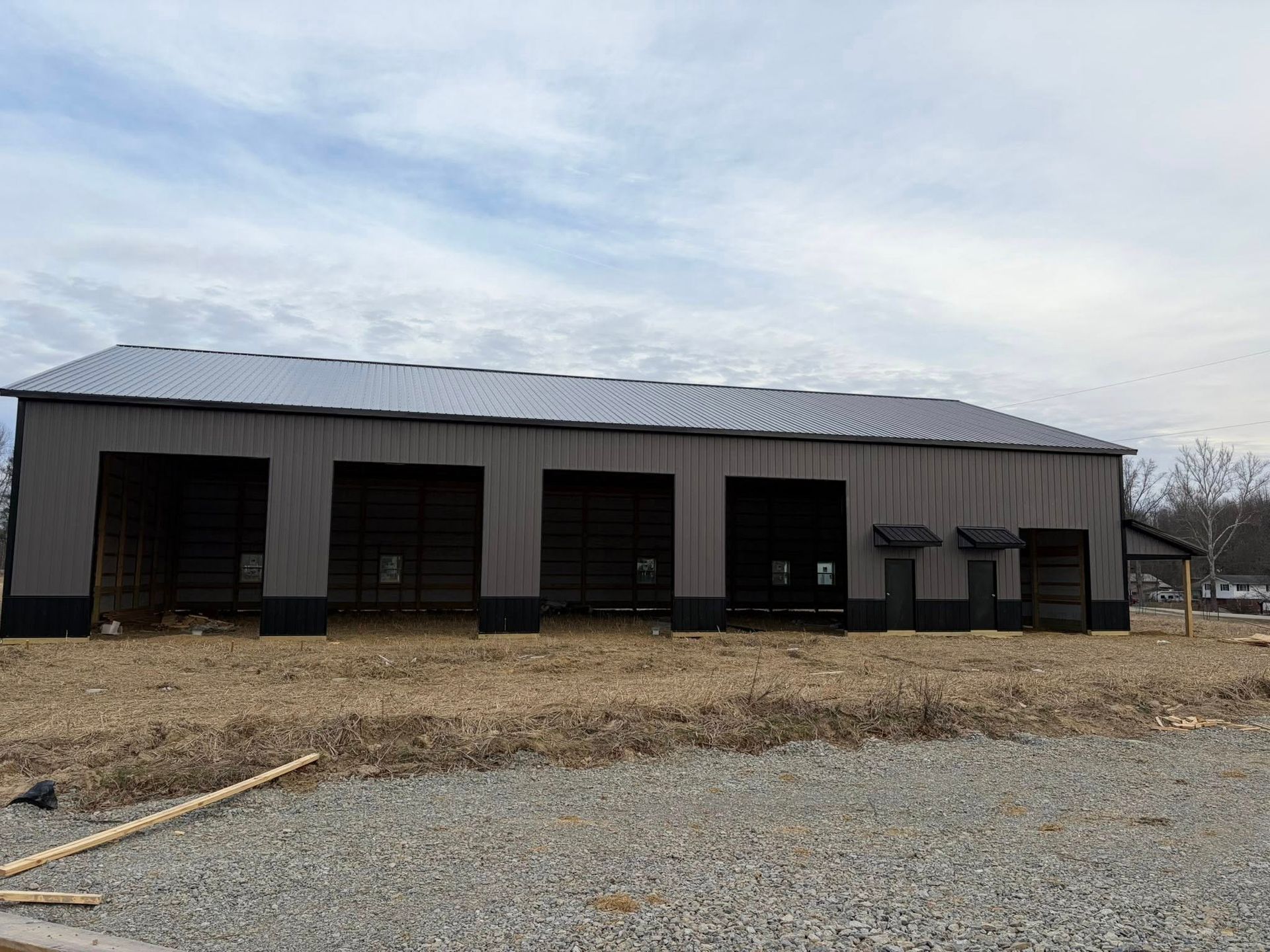 Gray metal barn with open bays on a gravel lot under a cloudy sky
