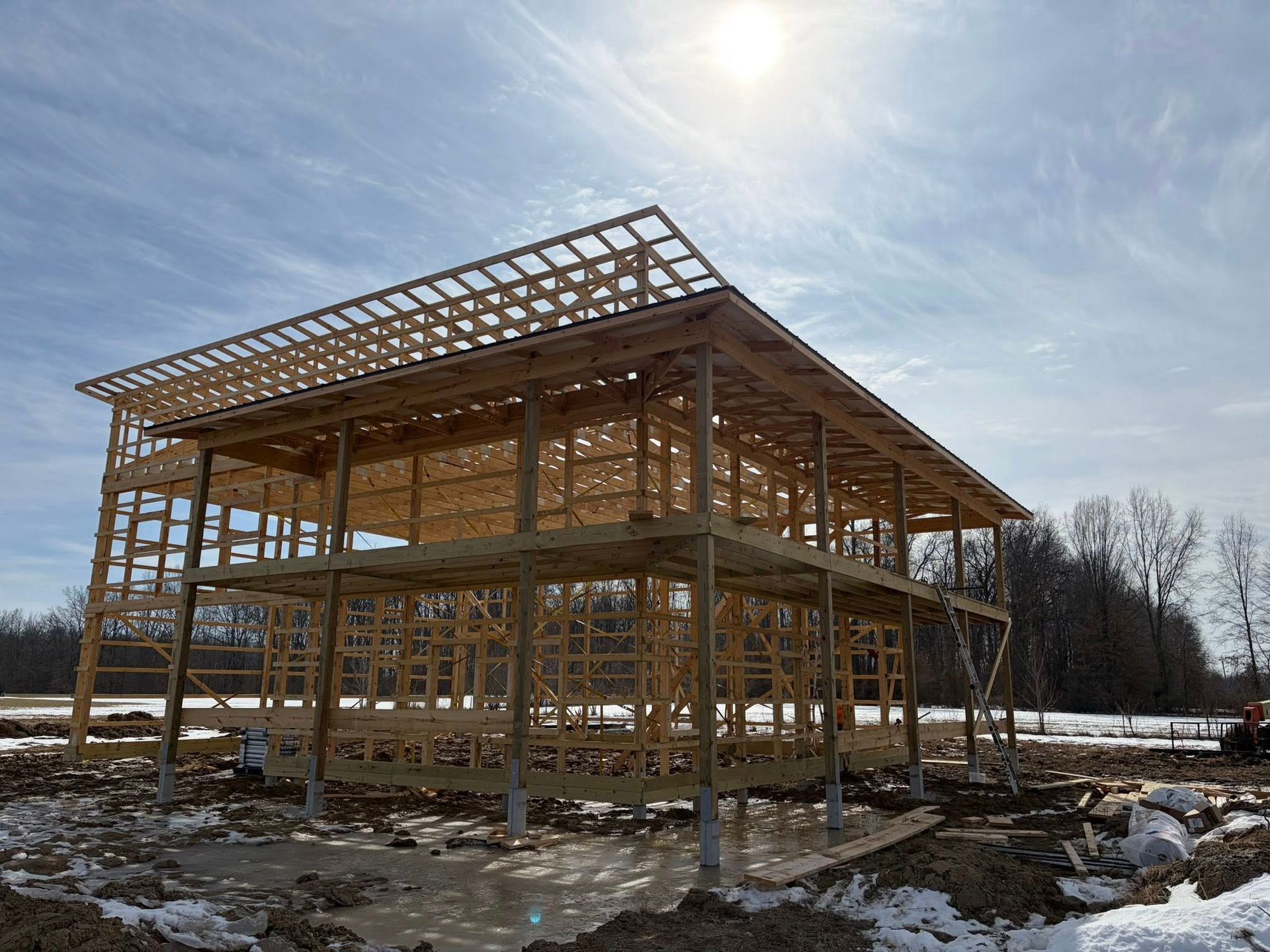 Wood-framed house under construction on a snowy lot beneath a bright sky