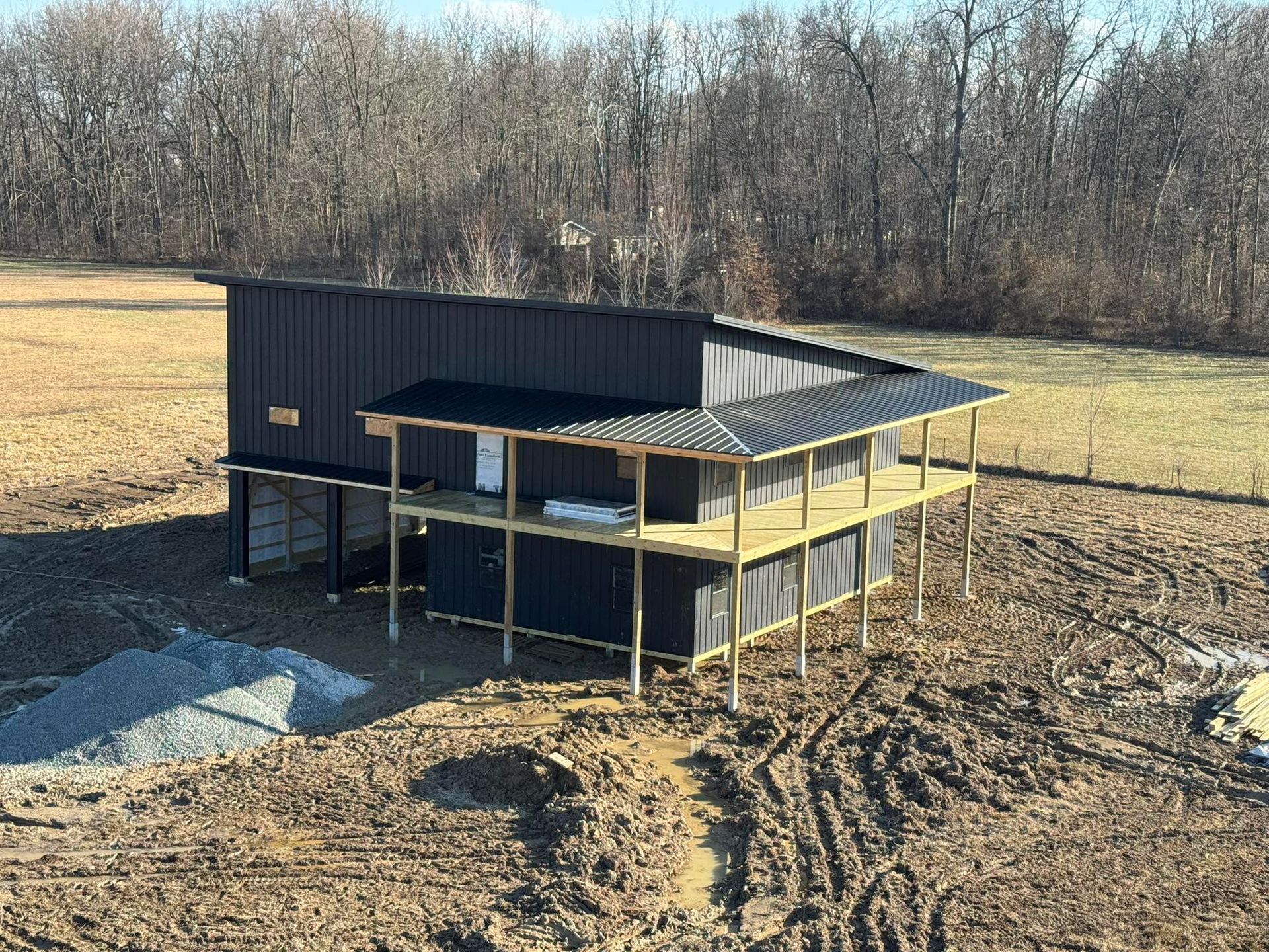 Small black shed under construction on a bare rural lot with wooden posts and gravel