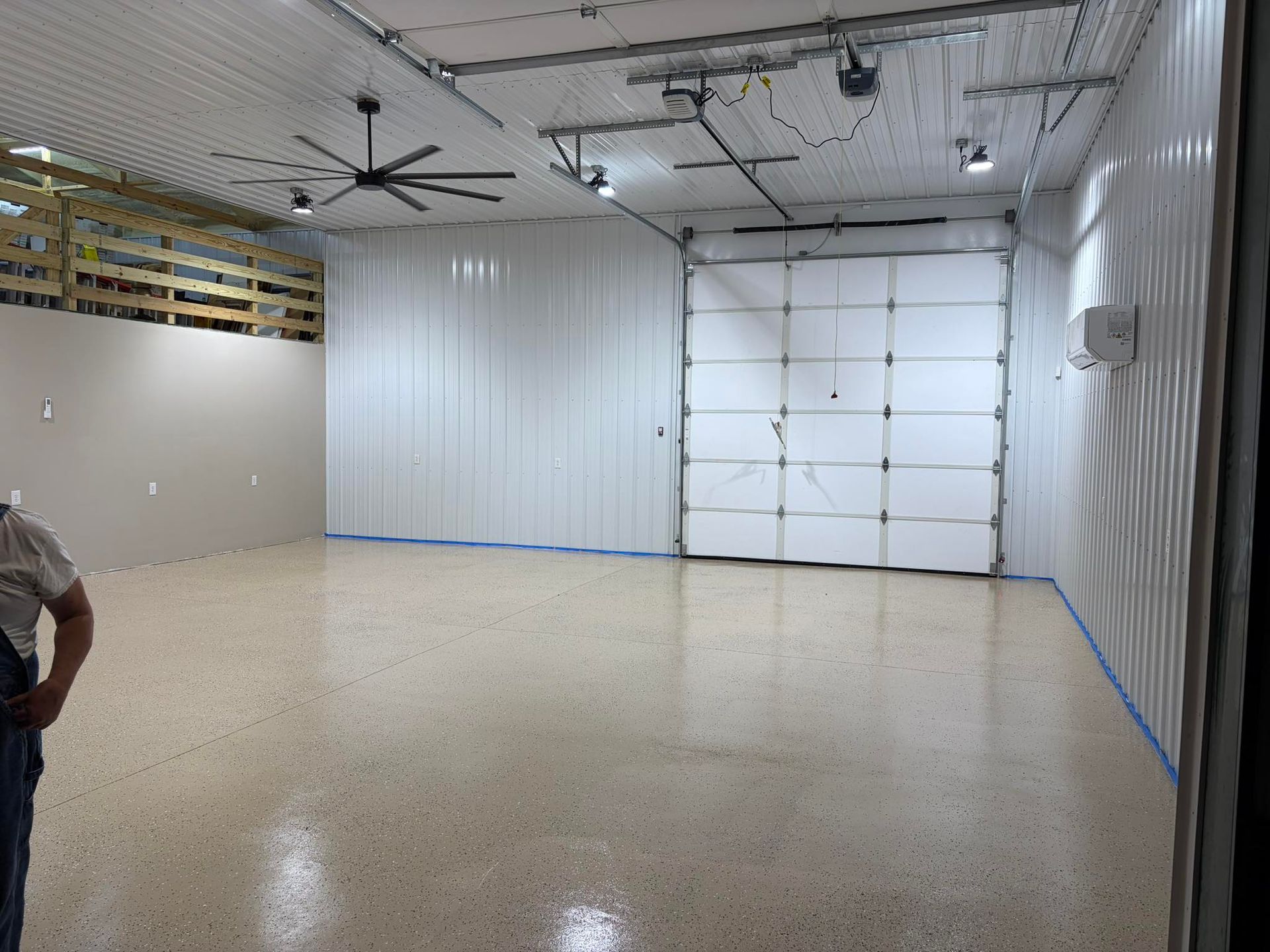 Empty indoor garage with white walls, overhead lights, and a large roll-up door