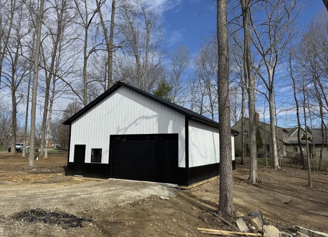 White garage or shed with black trim in a wooded yard under a clear blue sky