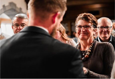 Audience members smiling at a speaker during a formal event, with a man in the foreground.