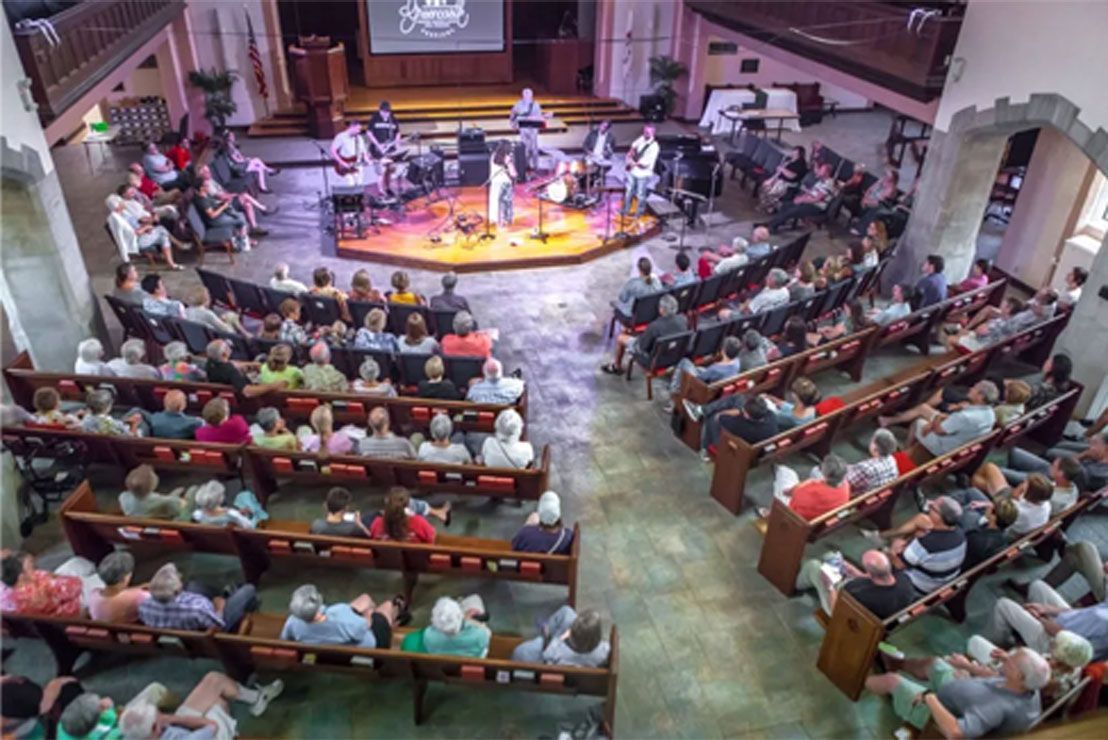 Wide view of a church sanctuary with a congregation seated around a central stage and band
