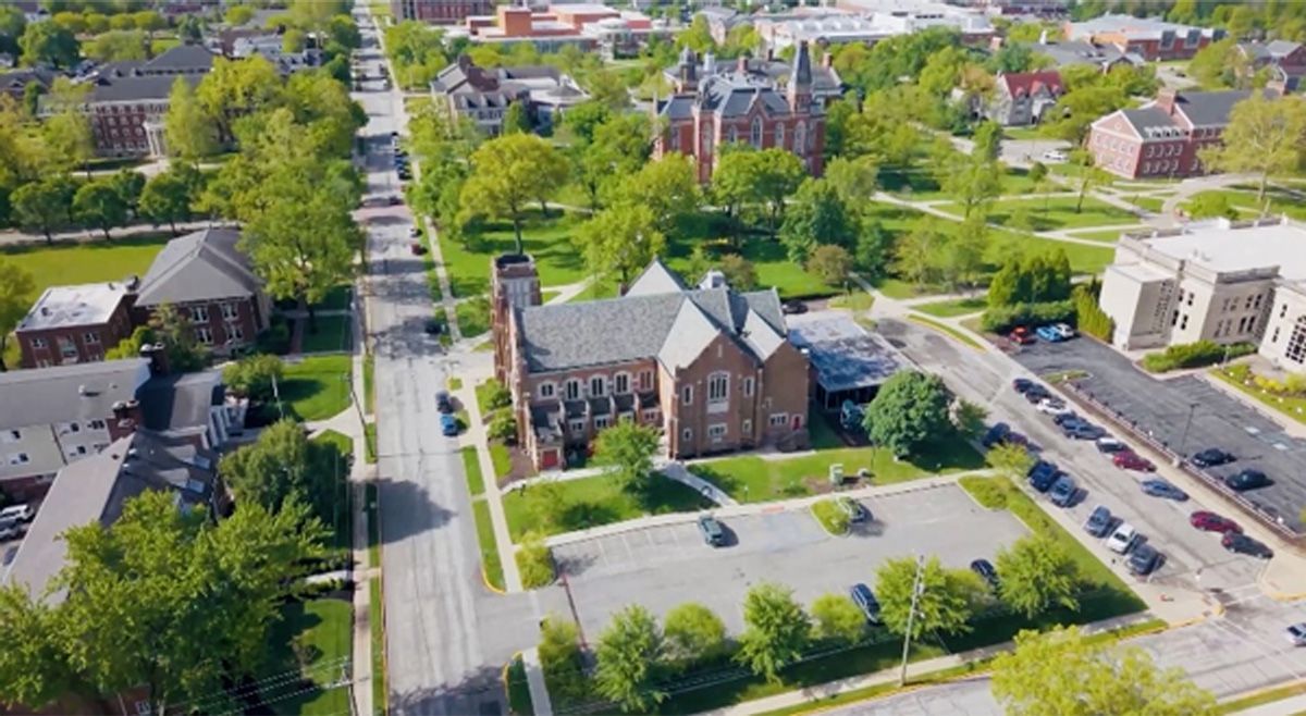 Aerial view of a brick building beside tree-lined streets and parking lots in a suburban neighborhood