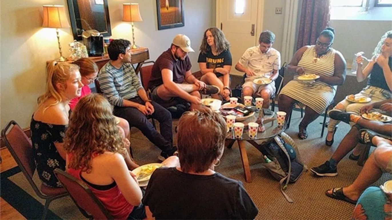 Group of people seated in a hotel lounge, chatting around a coffee table with drinks and snacks
