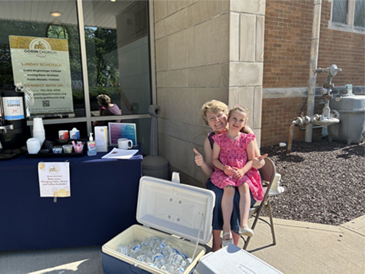 Woman and child seated outside a storefront beside a table with a cooler and display items