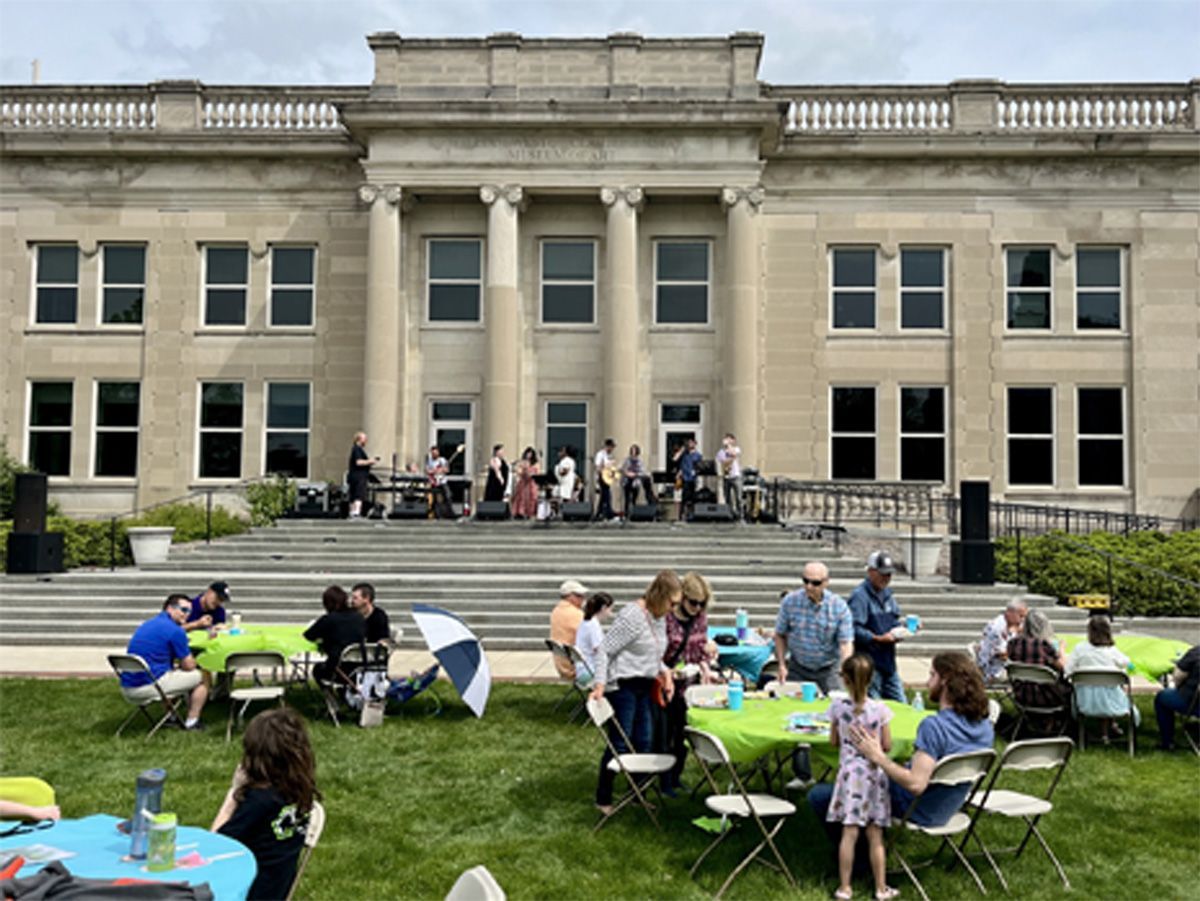 People sitting at tables on a lawn in front of a large stone building.