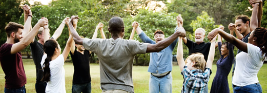 People standing in a circle outdoors with arms raised and linked in a group activity