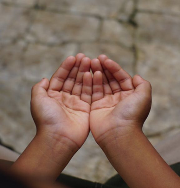 Two hands cupped together in a prayer-like gesture against a stone background