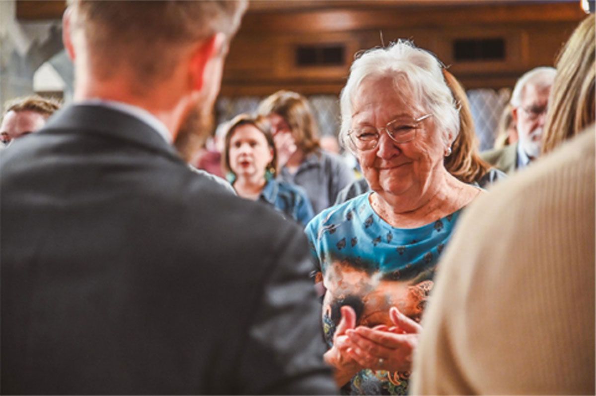 Smiling woman in a blue top chatting at a crowded indoor gathering