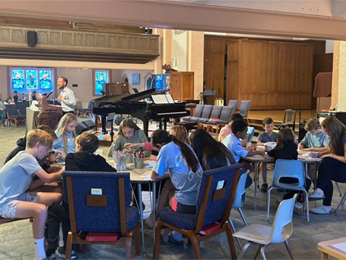 People seated in a music rehearsal room with a grand piano and music stands