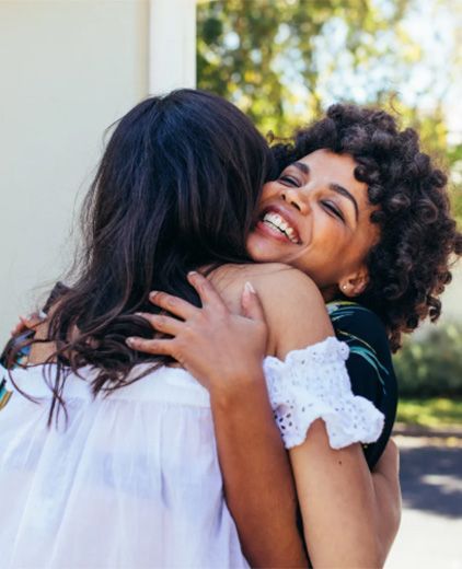 Two people hugging outdoors, one smiling broadly over the other’s shoulder.