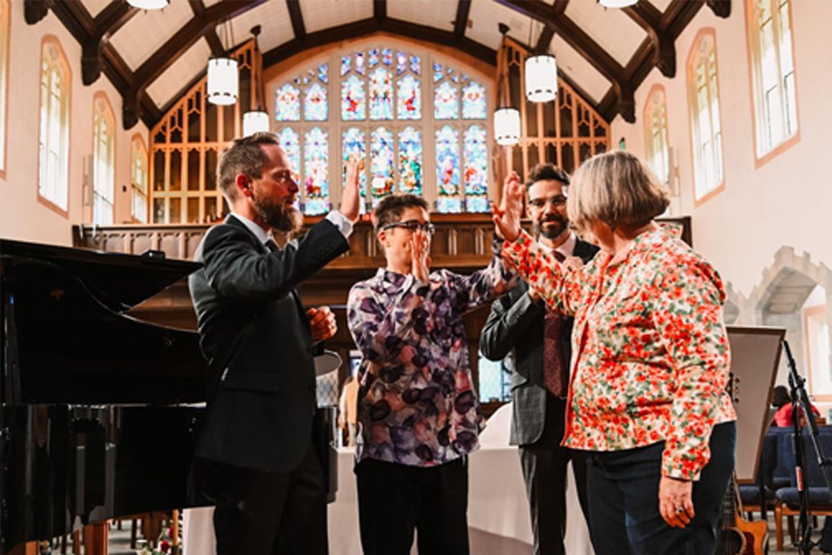 Four musicians in a church, raising glasses in celebration beside a grand piano.