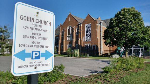 Roadside sign for Gobin Church beside a brick church building and parking lot under a blue sky