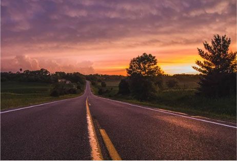 Empty road at sunset with a pink-orange sky and trees on both sides