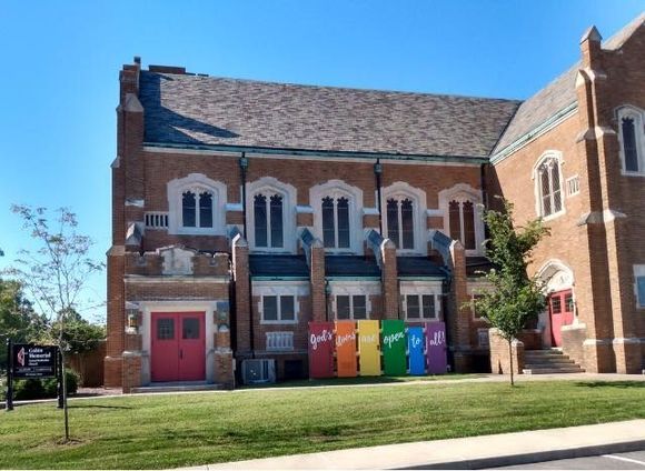 Brick building with red door and colorful bins along the front, beside a grassy lawn under a blue sky