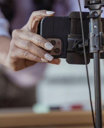 Hand adjusting a smartphone on a tripod for filming in a blurred indoor setting