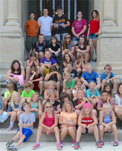 Large group posing on stone steps outside a building, many smiling and seated in rows