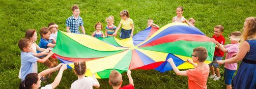 Children holding a colorful parachute outdoors in a circle, playing together on grass.