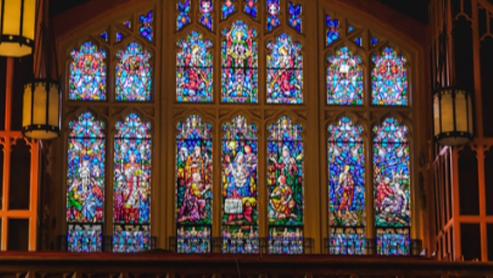 Colorful stained-glass church window with a central religious scene and ornate wooden framing