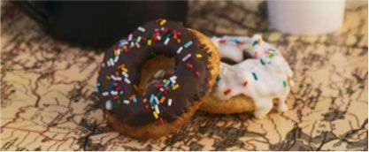 Two chocolate-frosted donuts with sprinkles on a countertop, one with white icing