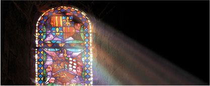 Colorful stained-glass window casting bright sunlight into a dark room