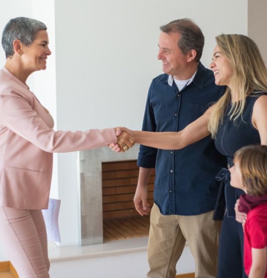 Two people shaking hands in a bright room, with a smiling man and child nearby.