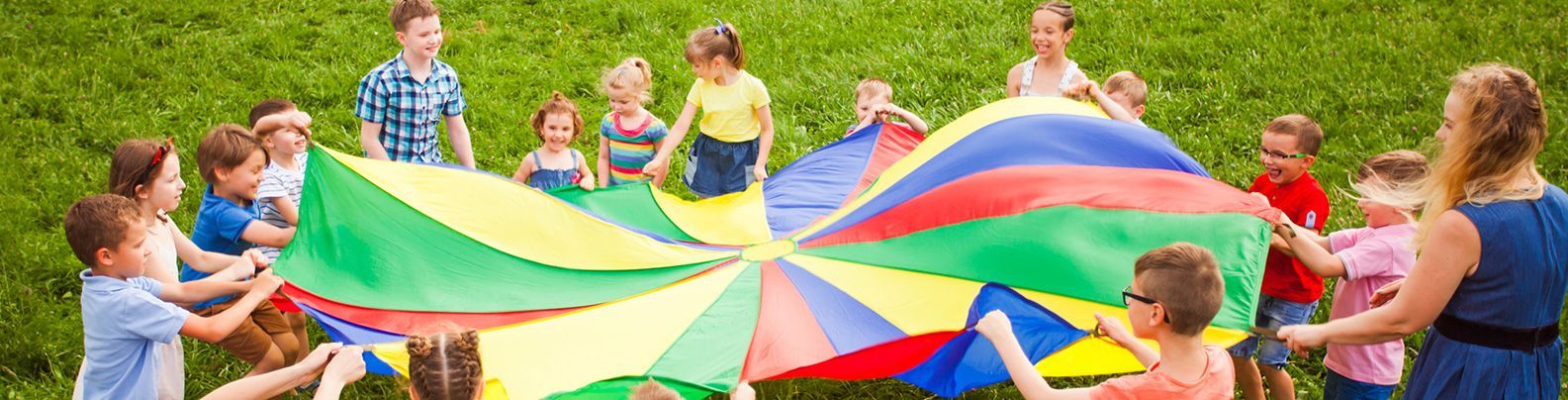 Children hold a colorful parachute in a grassy field, playing together outdoors.