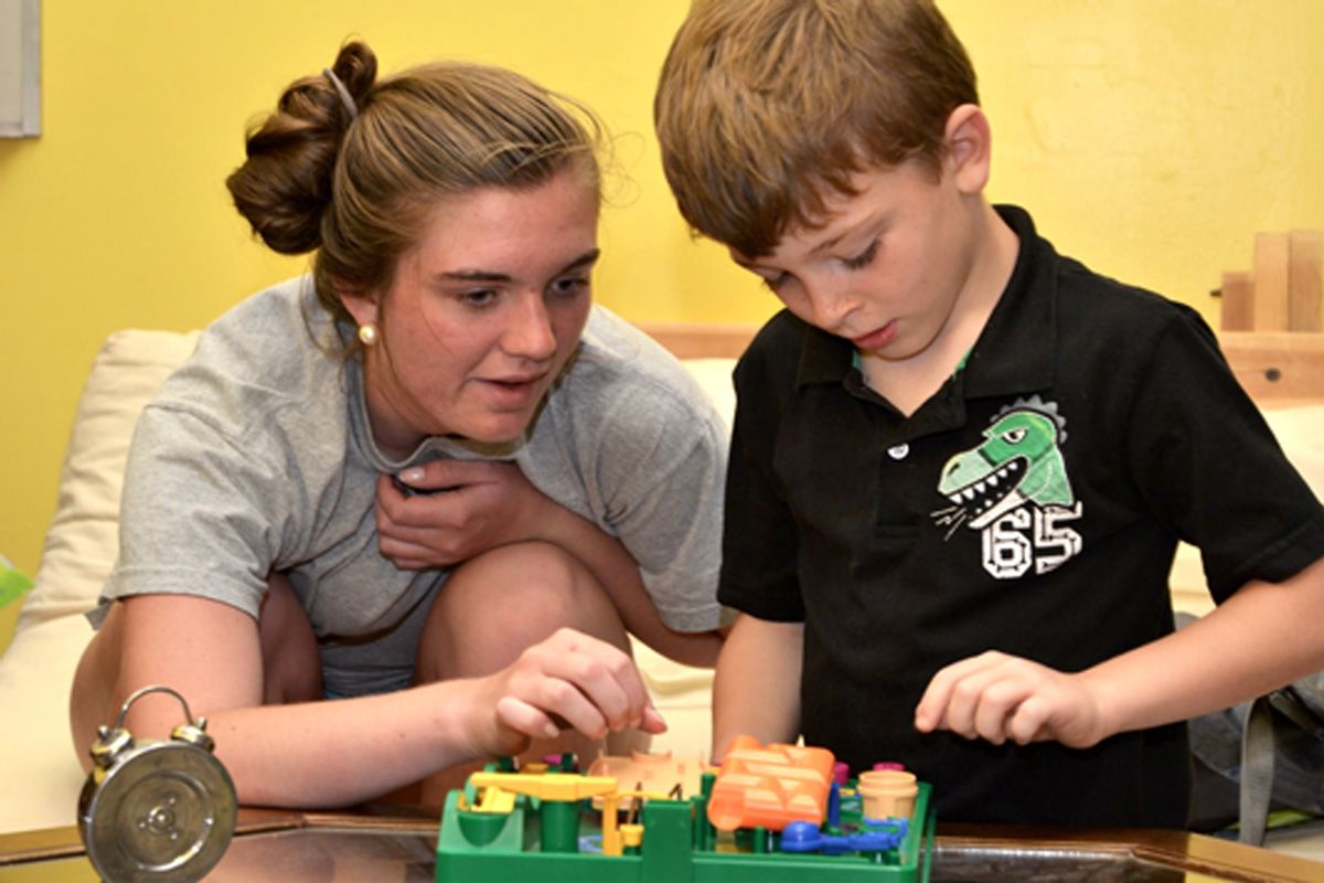 Woman and boy lean over a colorful toy set on a table, concentrating together.