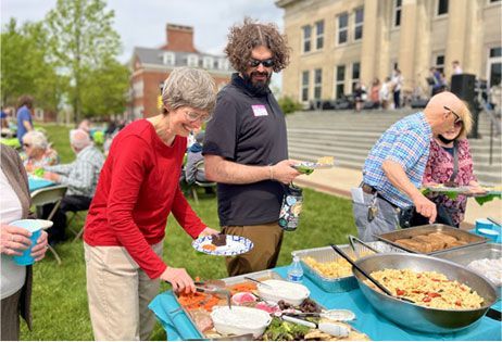 People serving food at an outdoor community buffet table in a park