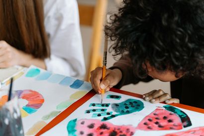 Iemand concentreert zich intensief terwijl hij met een penseel watermeloen- en kleurencirkelpatronen op papier schildert.