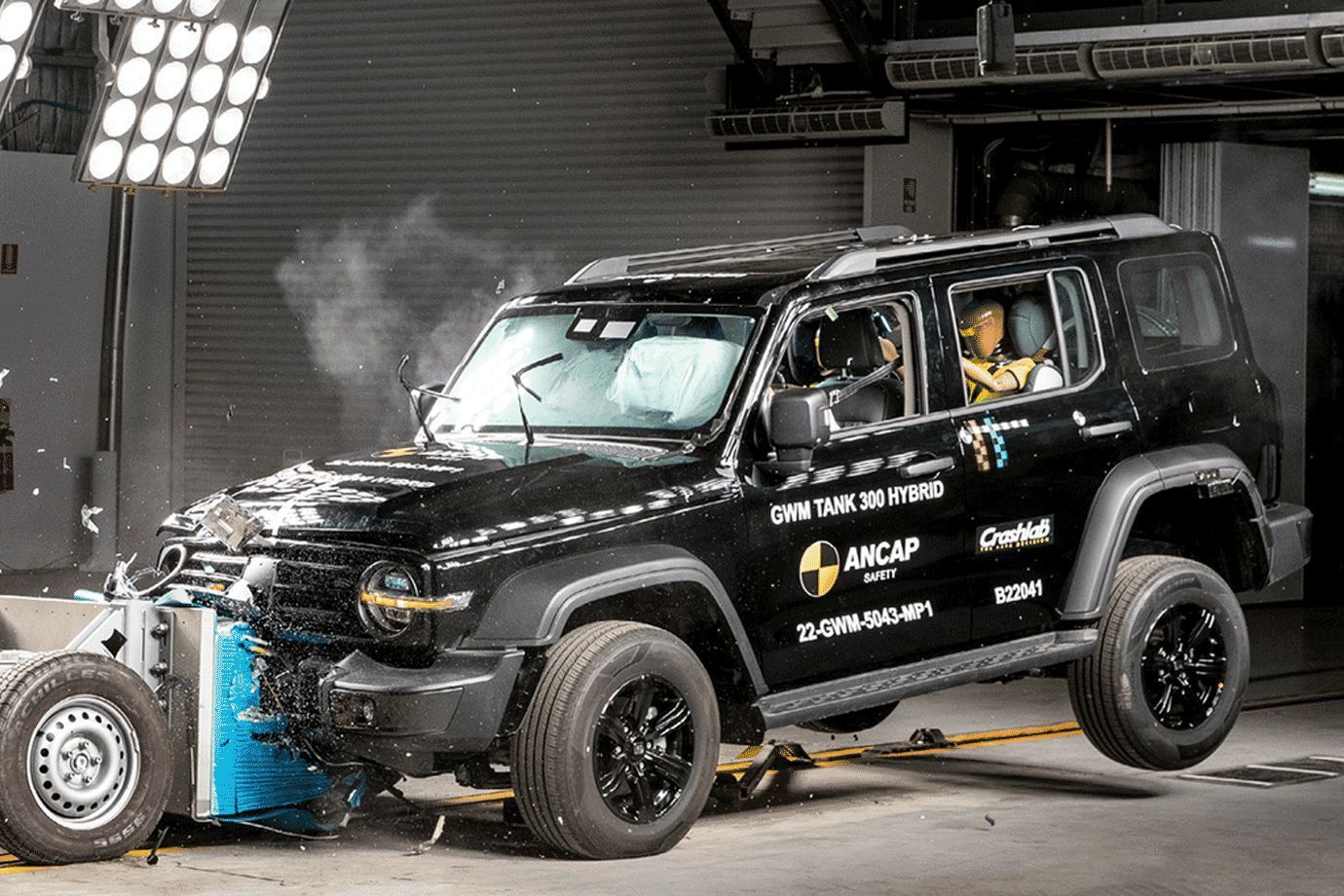 SUV negro con el frontal abollado en un centro de pruebas de choque, con humo saliendo del capó