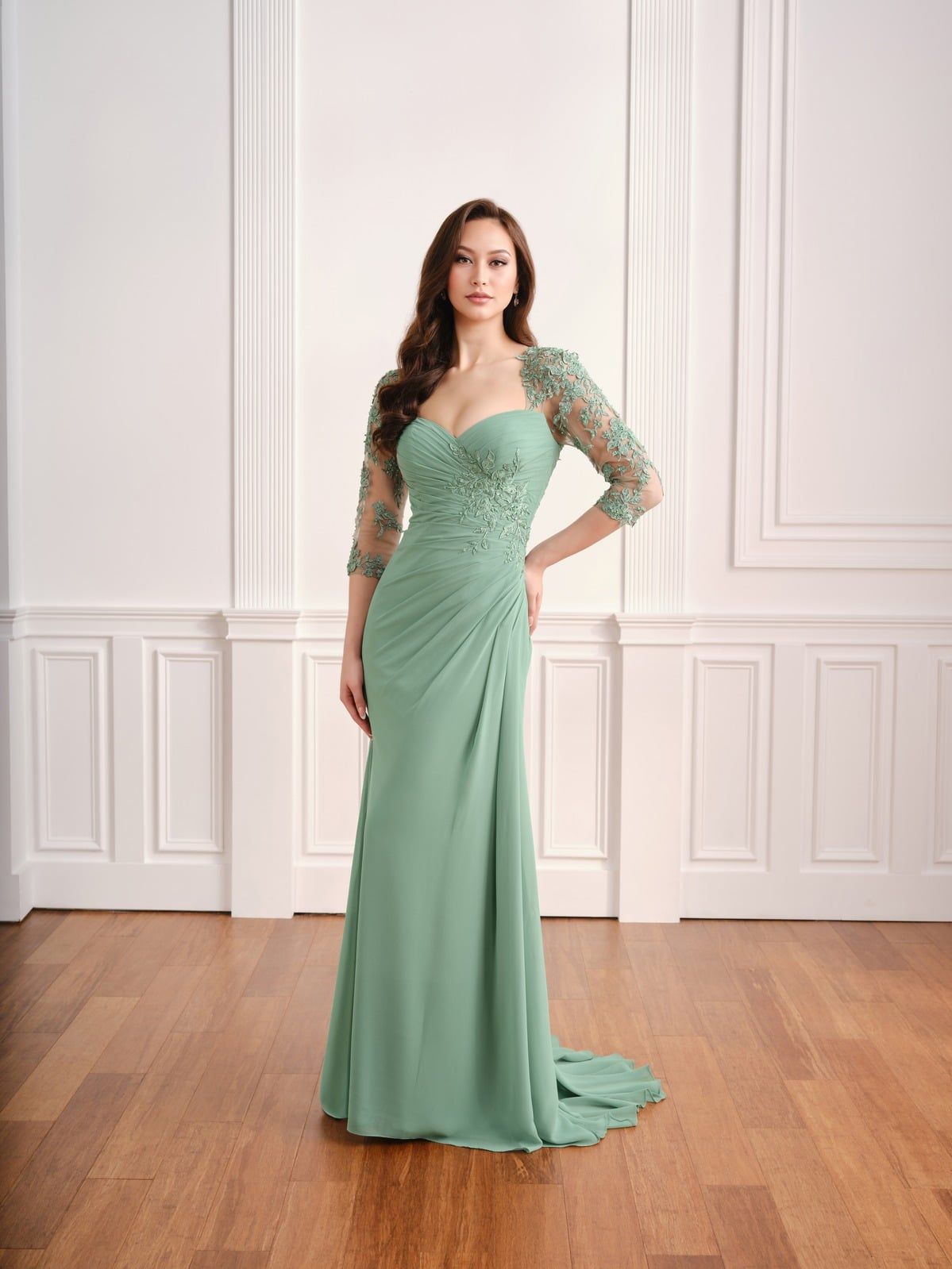 Woman in a mint green gown posing in a white-paneled room with wood floors