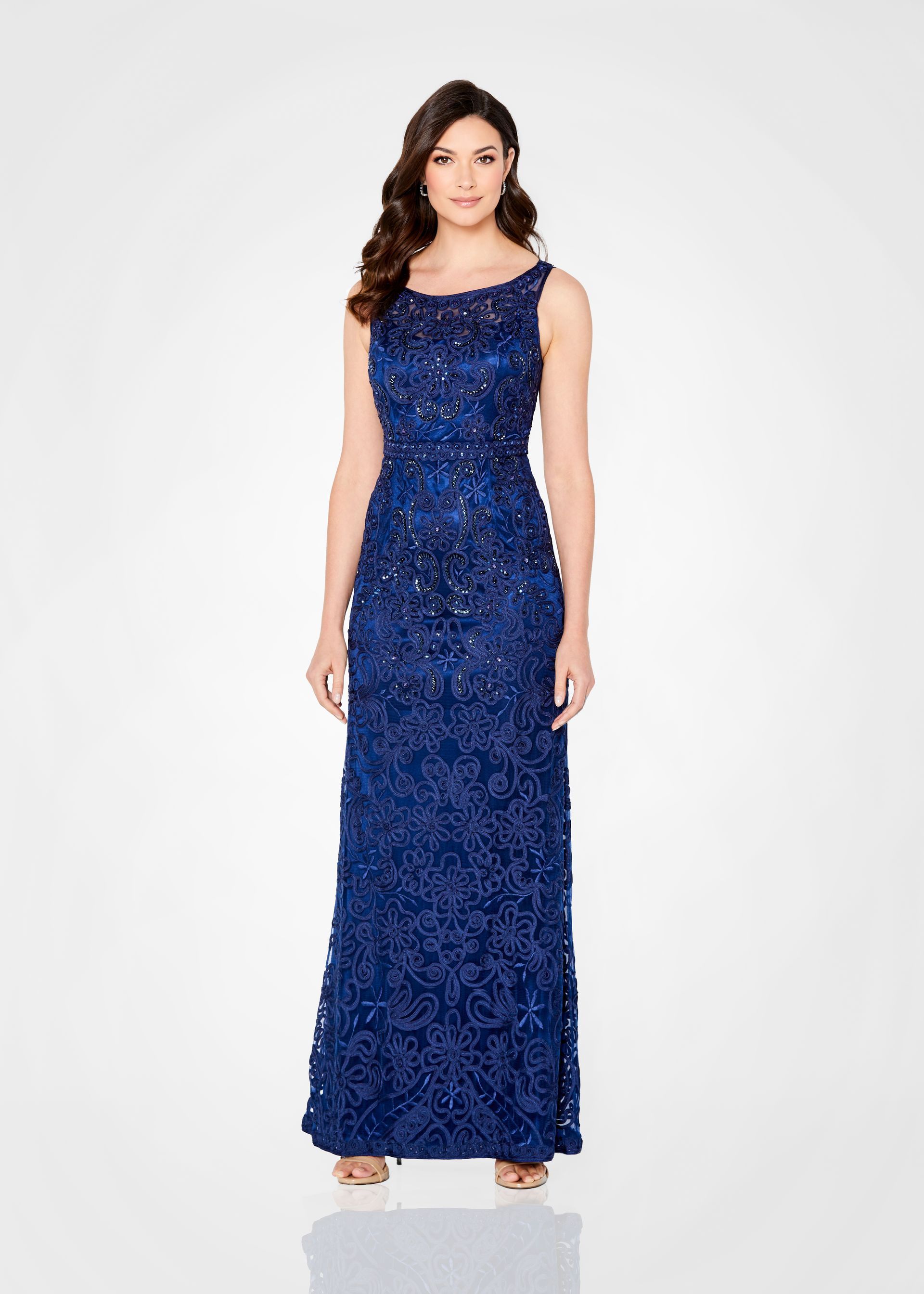 Woman in a navy blue floor-length gown with intricate beadwork, standing in front of a white background.