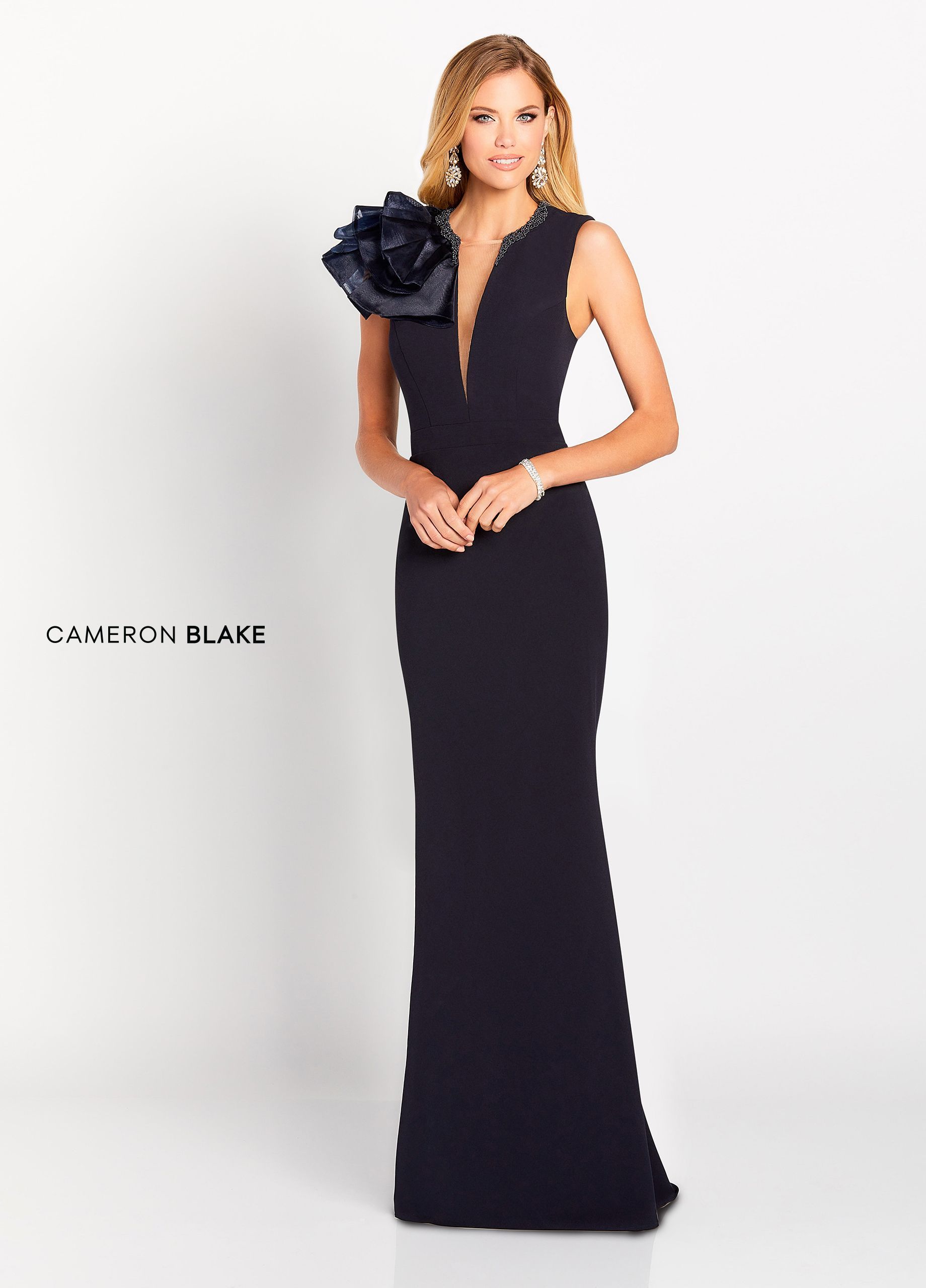 Woman in a black gown with a large floral shoulder detail, standing indoors.