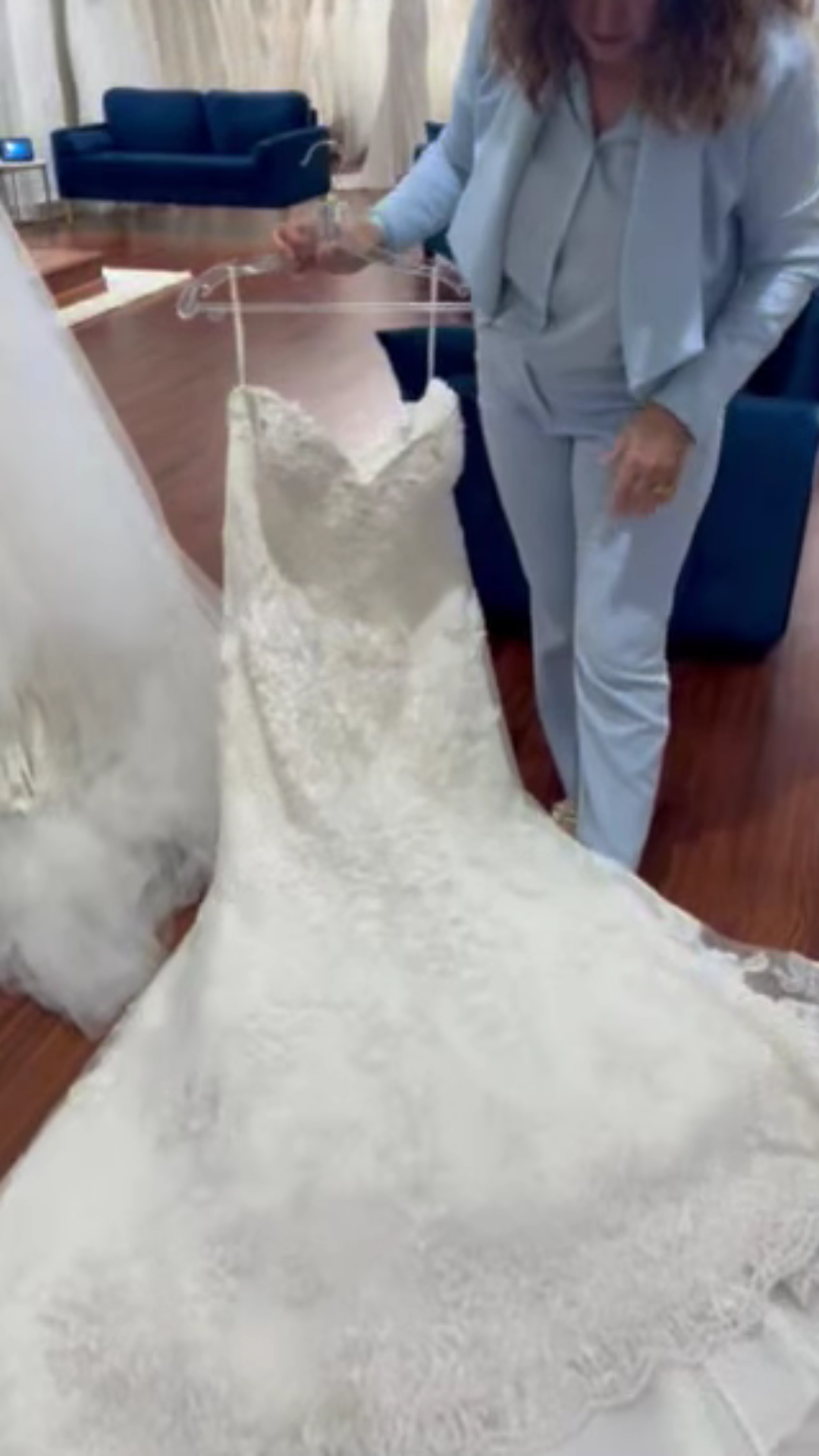 Person holding a white lace wedding dress in a room with hardwood floors and blue seating
