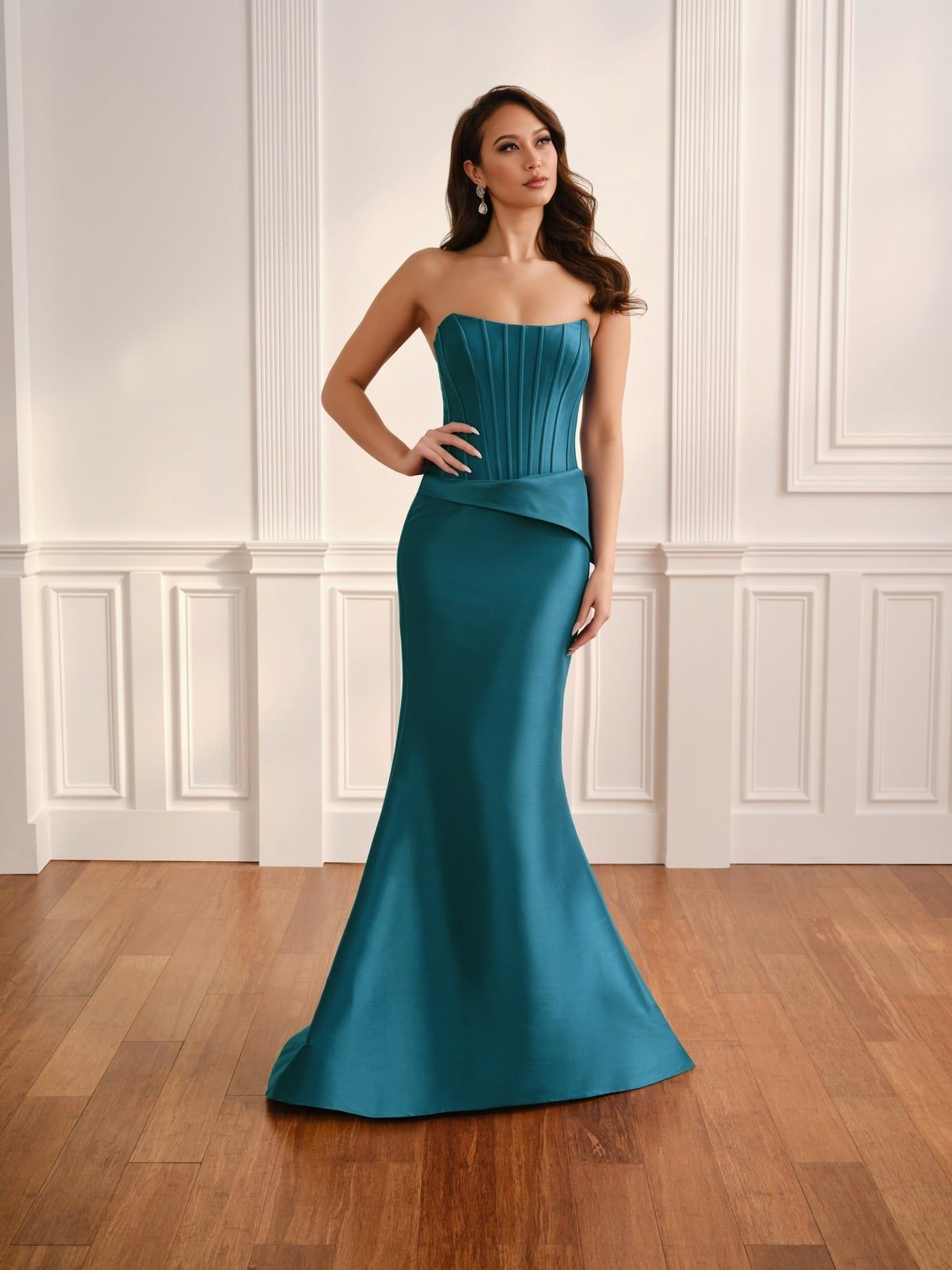 Woman in a teal strapless evening gown standing in a white-paneled room with hardwood floors