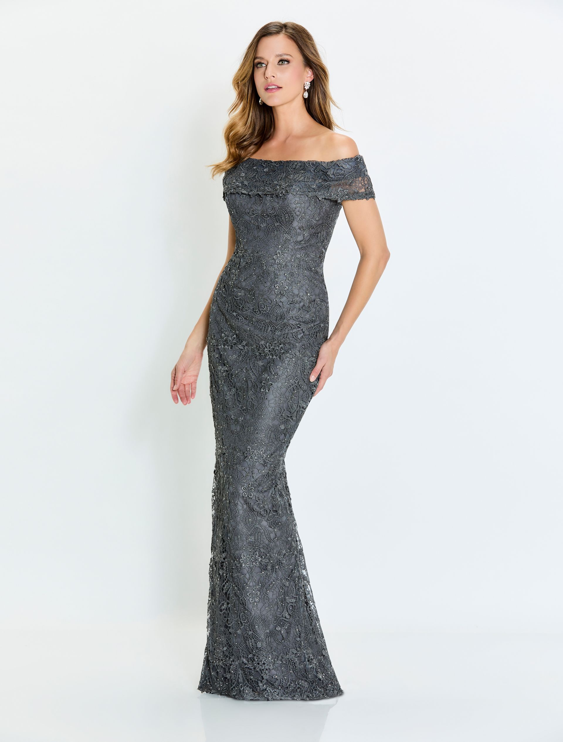 Woman in a gray, beaded, off-the-shoulder formal gown, posing indoors.