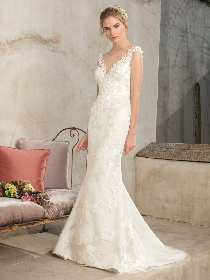 Woman in a white lace mermaid wedding dress, posing in front of an outdoor wall.
