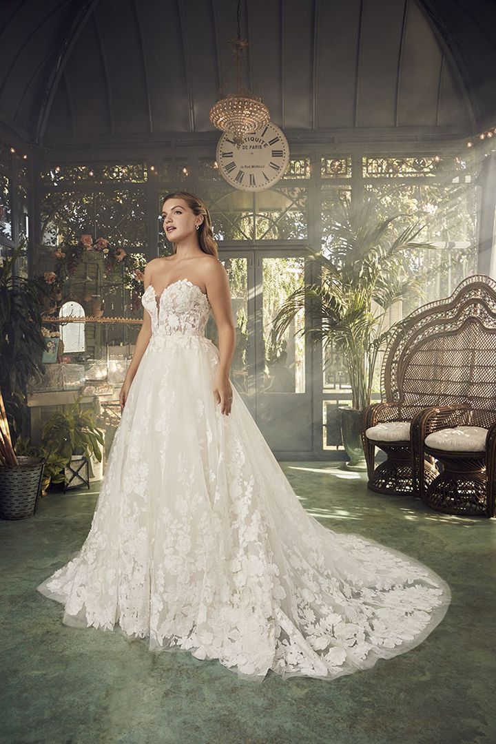 Woman in a strapless white lace wedding dress poses in an ornate greenhouse.