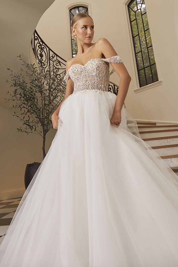 Woman in wedding dress on staircase, off-the-shoulder bodice, full skirt, holding fabric.