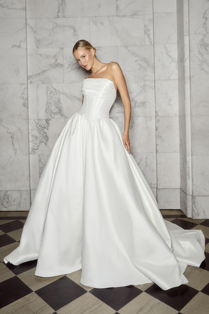 Woman in strapless white satin ball gown posing against marble wall.