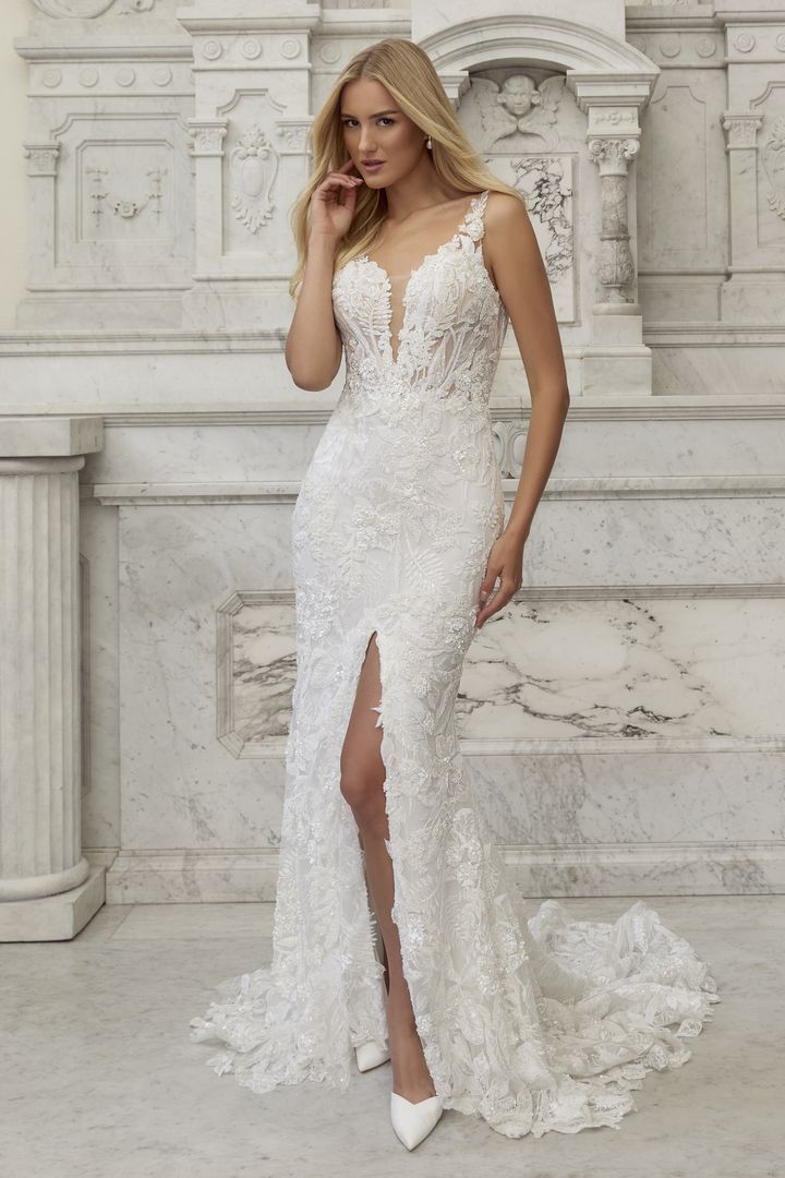 Woman in a white lace wedding dress with a thigh-high slit, posing in front of a marble wall.