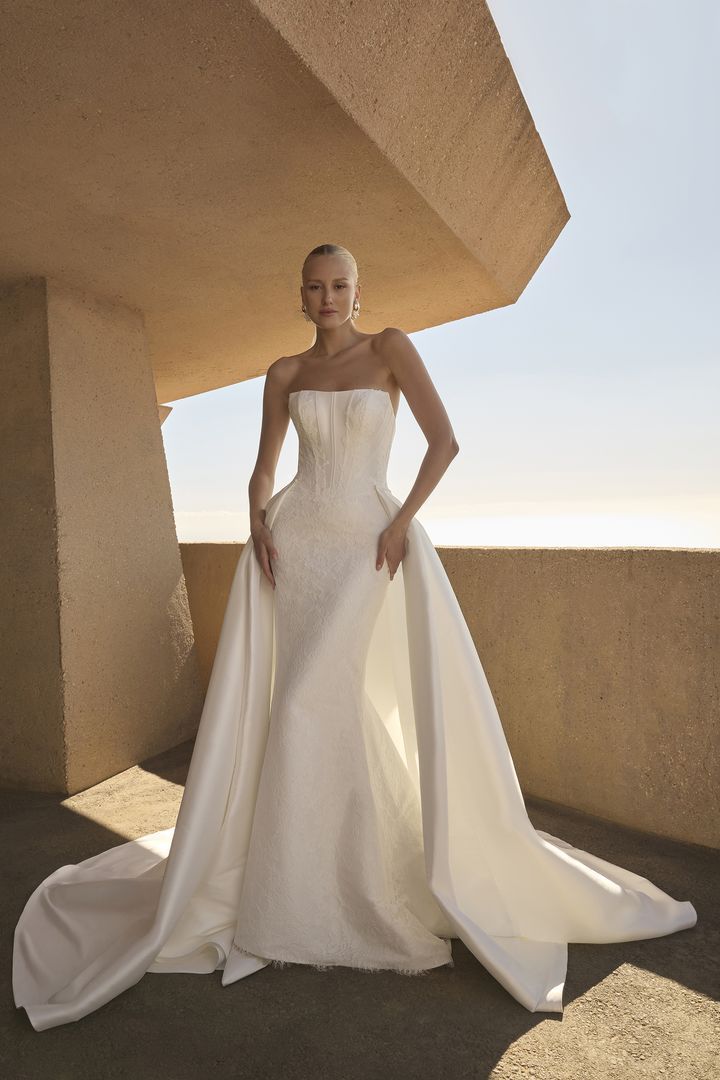 Woman in a strapless white wedding dress with detachable train, standing on a balcony.