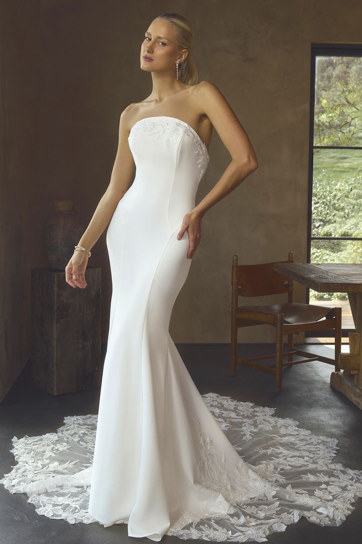 Bride in a strapless white gown standing in a rustic room with a lace train. Bride in a strapless white gown standing in a rustic room with a lace train.