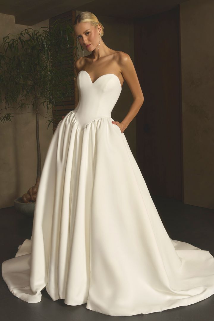 Woman in white wedding dress with a long train, standing near a waterfall, looking over her shoulder.