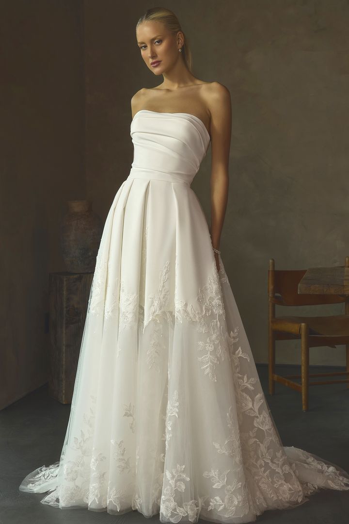 Woman in a strapless white wedding gown standing beside a chair against a dark backdrop Woman in a strapless white wedding gown standing beside a chair against a dark backdrop