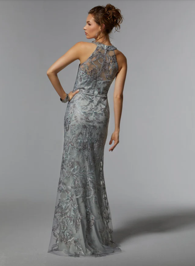 Woman in silver beaded gown, posing with hand on hip. Gray background.